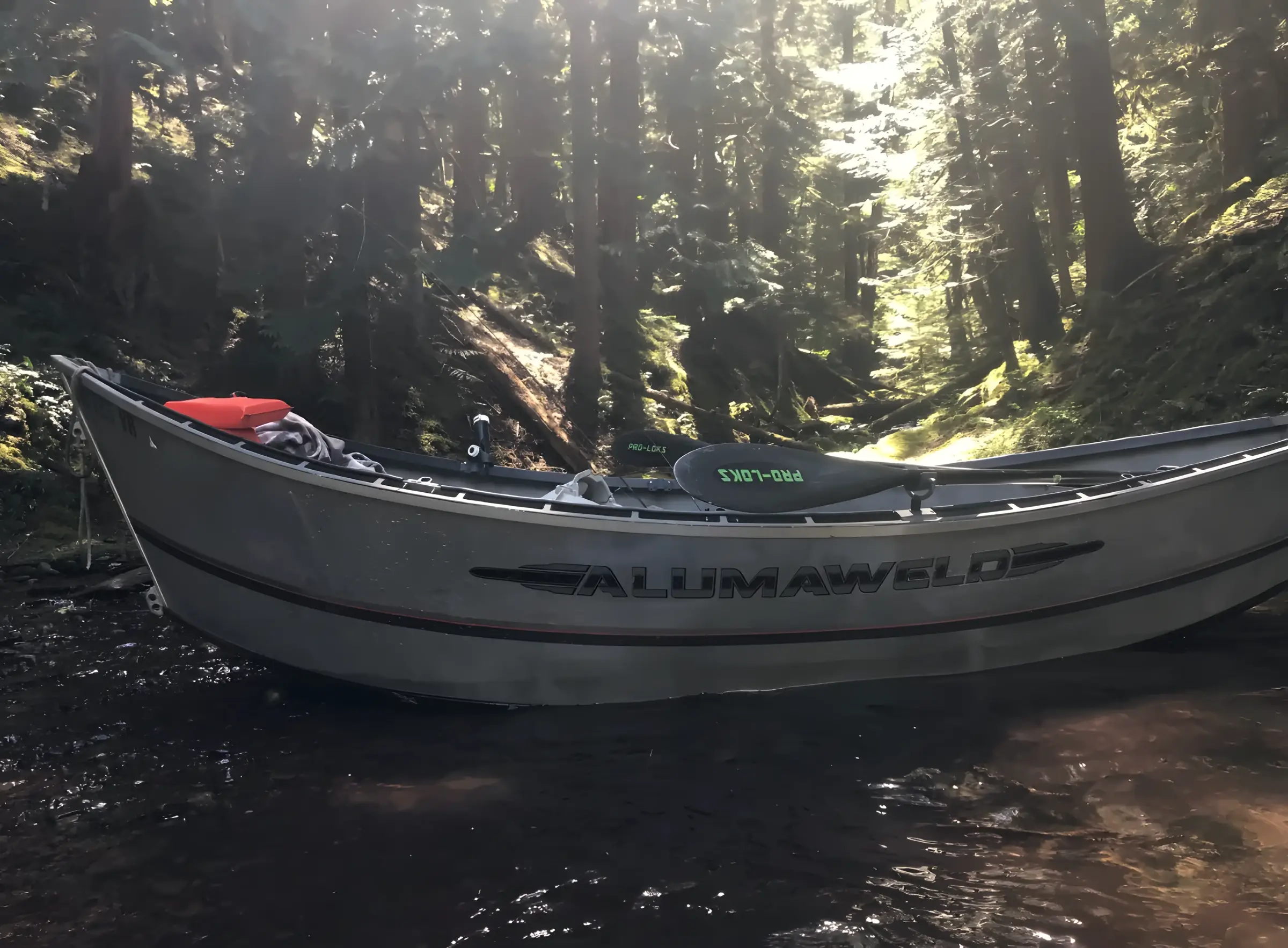 Aluminium drift boat with Alumaweld lettering resting on a forest stream