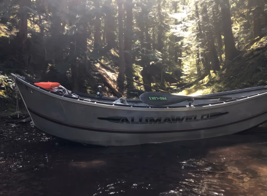 Aluminium drift boat with Alumaweld lettering resting on a forest stream