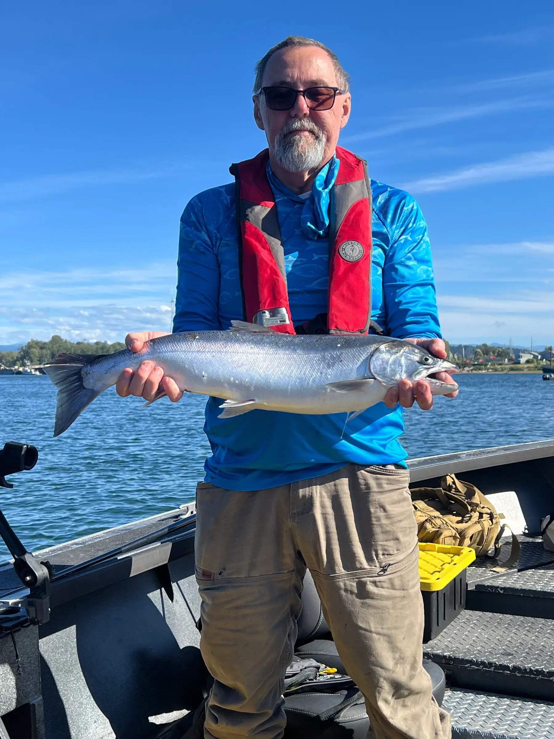 Angler in a blue shirt and life vest holding a bright silver fish under a clear sky