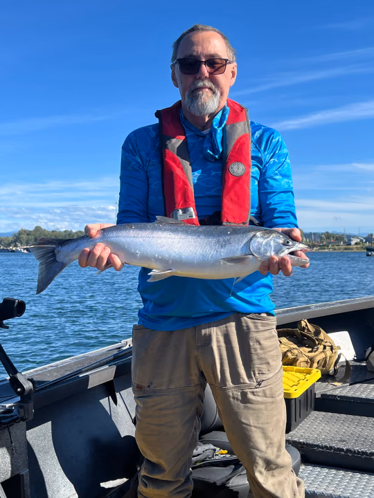 Angler in a blue shirt and life vest holding a bright silver fish under a clear sky