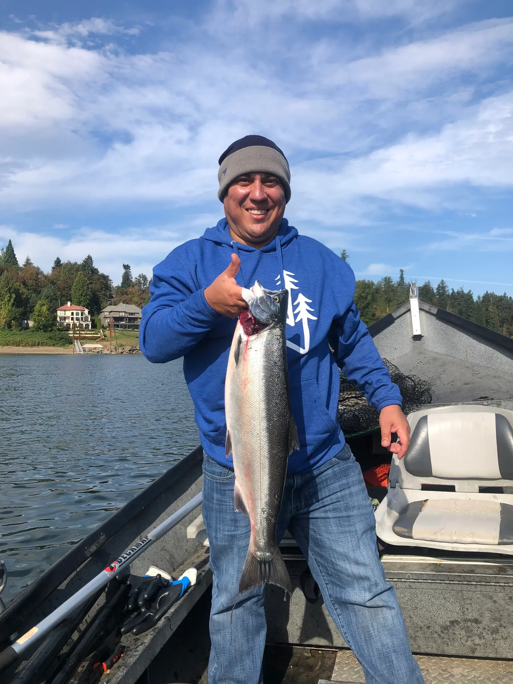 Angler in a blue hoodie on a boat holding a large fish and giving a thumbs up