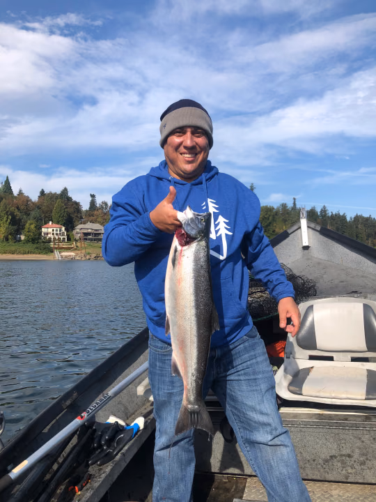 Angler in a blue hoodie on a boat holding a large fish and giving a thumbs up