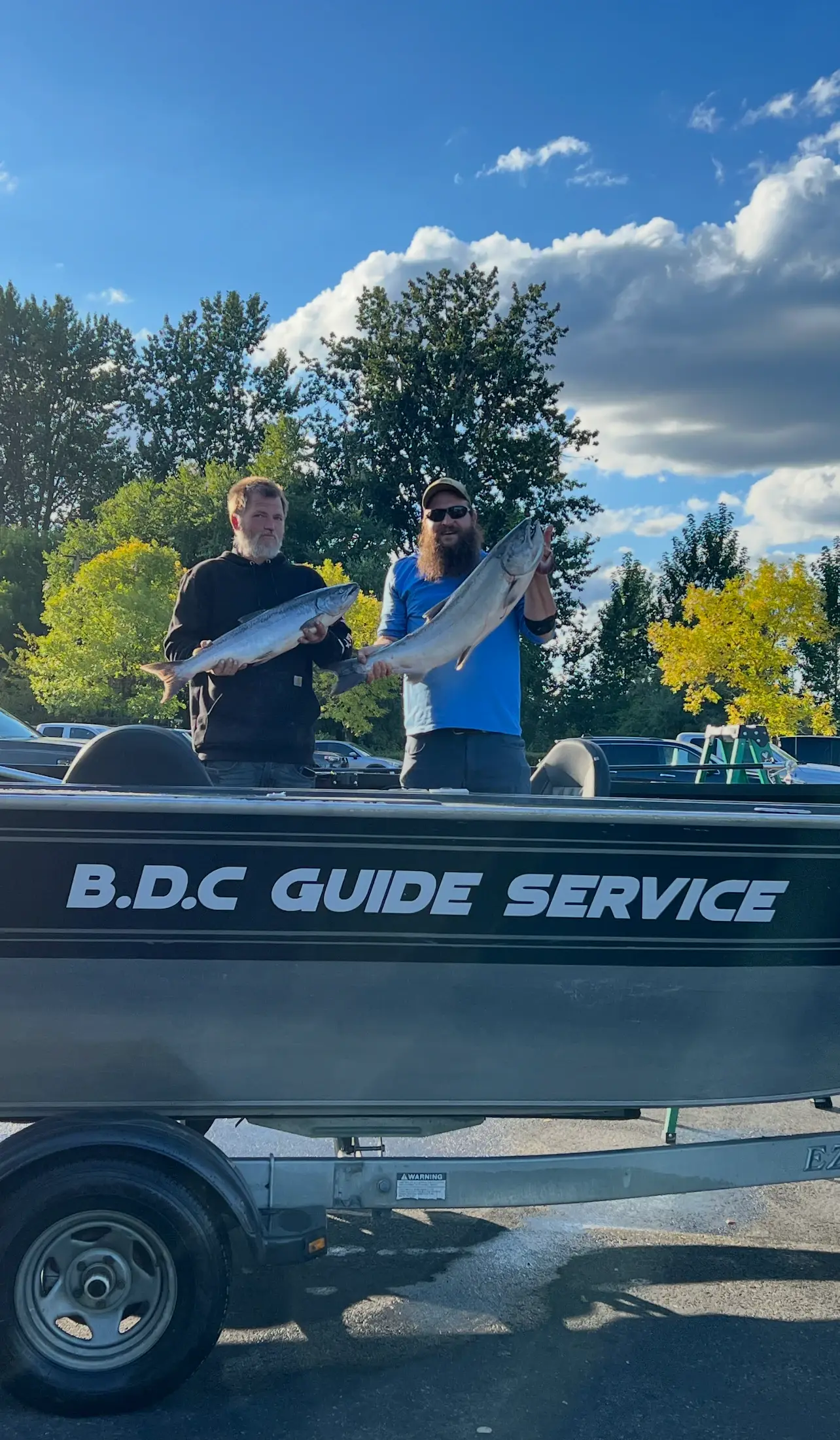 Two anglers standing in the BDC Guide Service boat on its trailer, each holding a fish