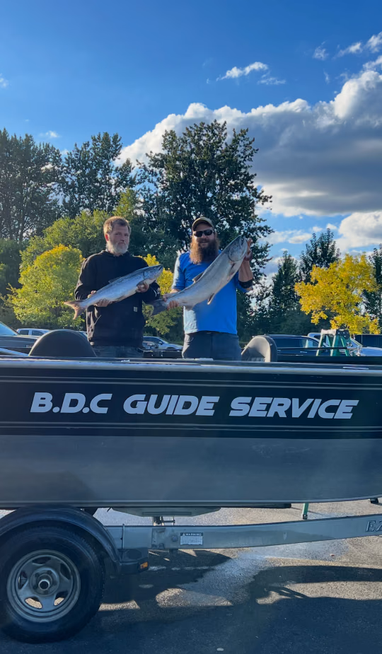 Two anglers standing in the BDC Guide Service boat on its trailer, each holding a fish