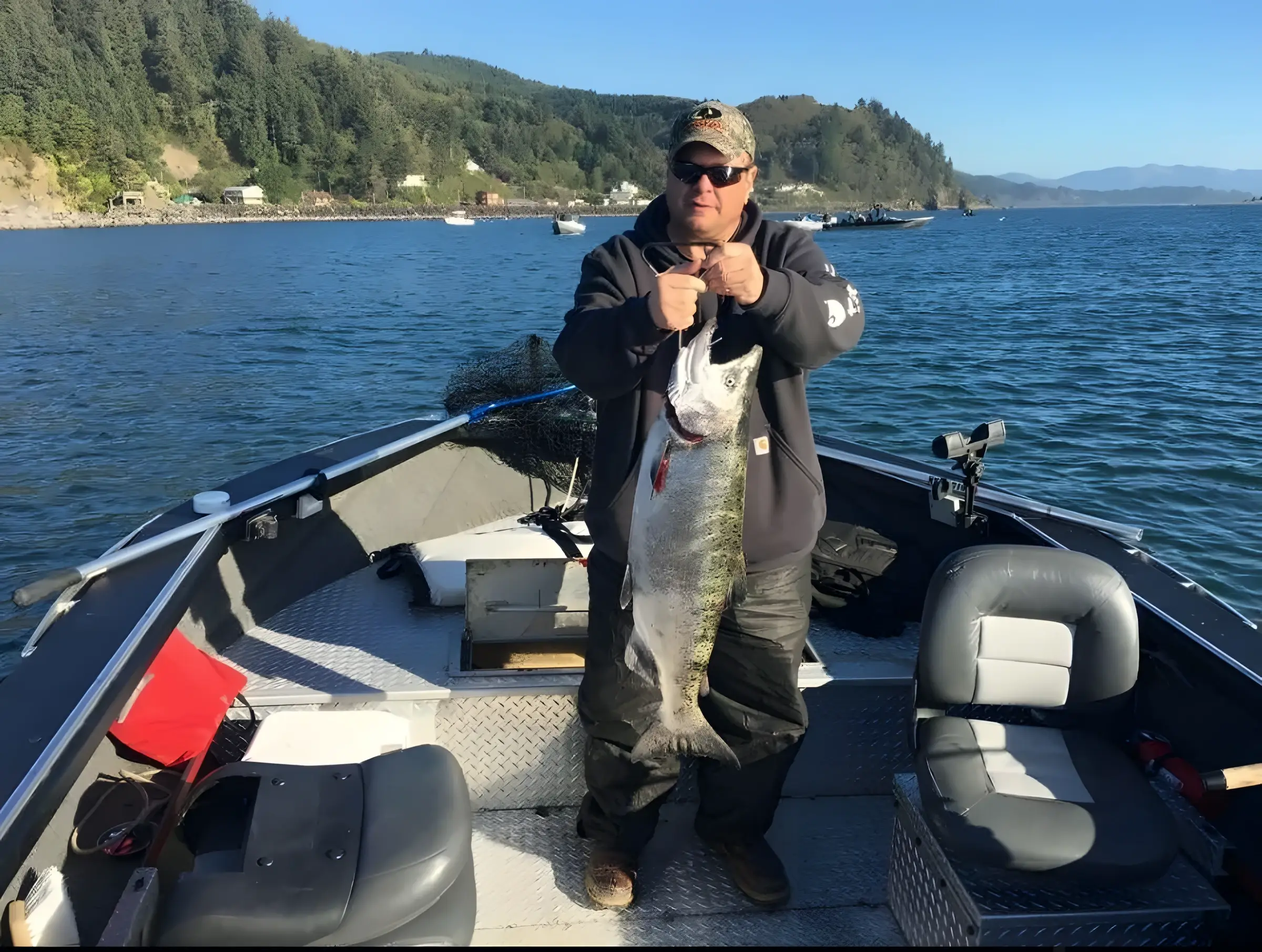 Angler on a boat holding a large fish with hills and open water behind