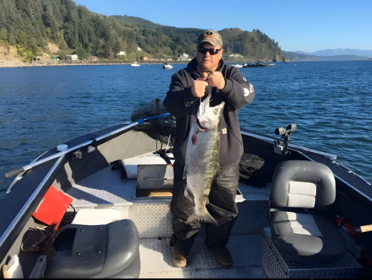 Angler on a boat holding a large fish with hills and open water behind
