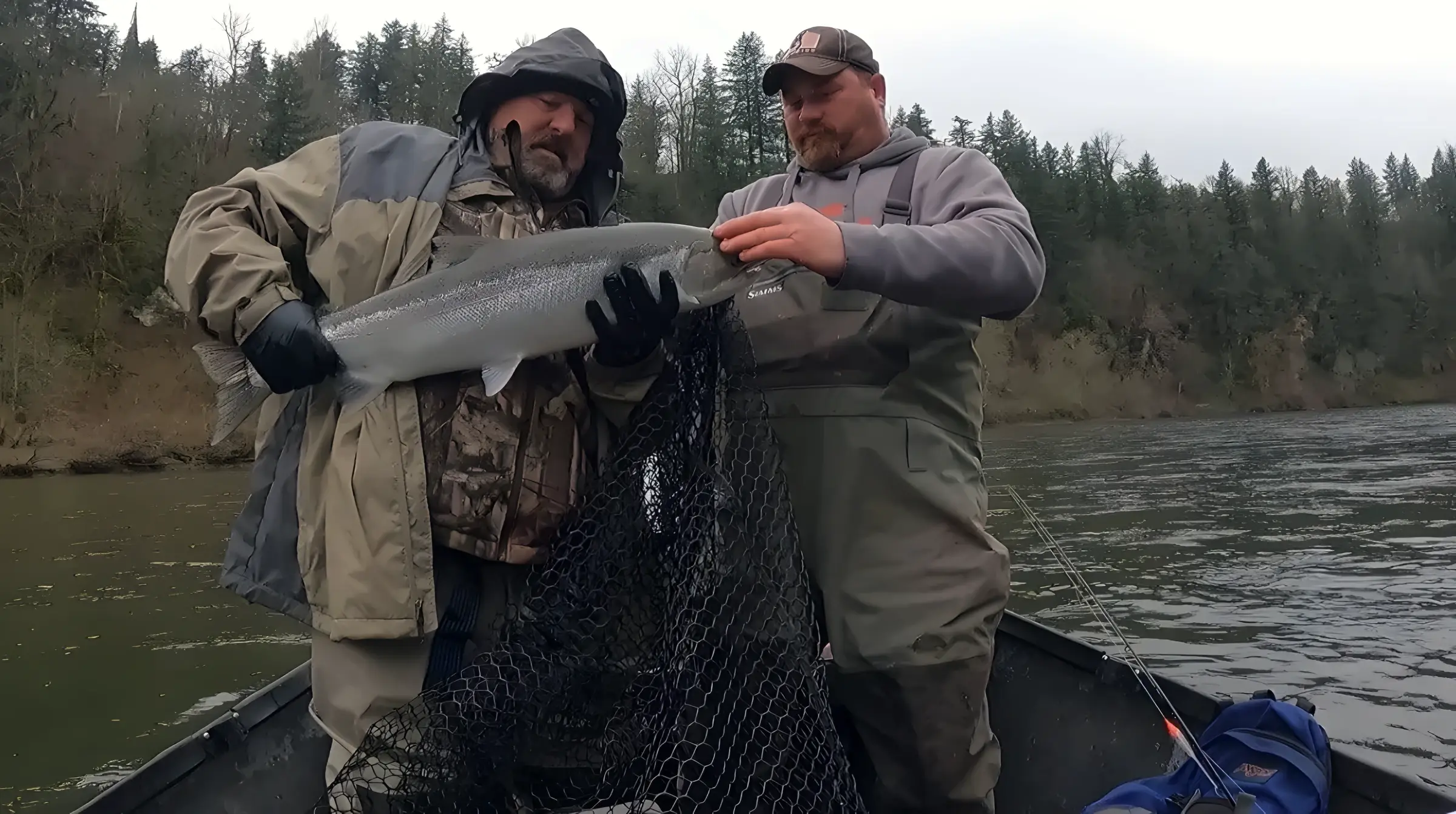 Two anglers in waders lifting a fish with a landing net on a boat