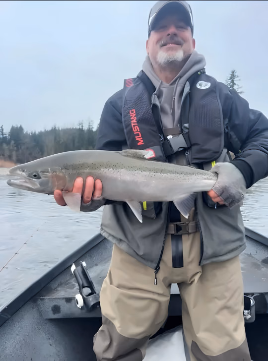 Angler in a life vest holding a large silver fish in a boat on the river
