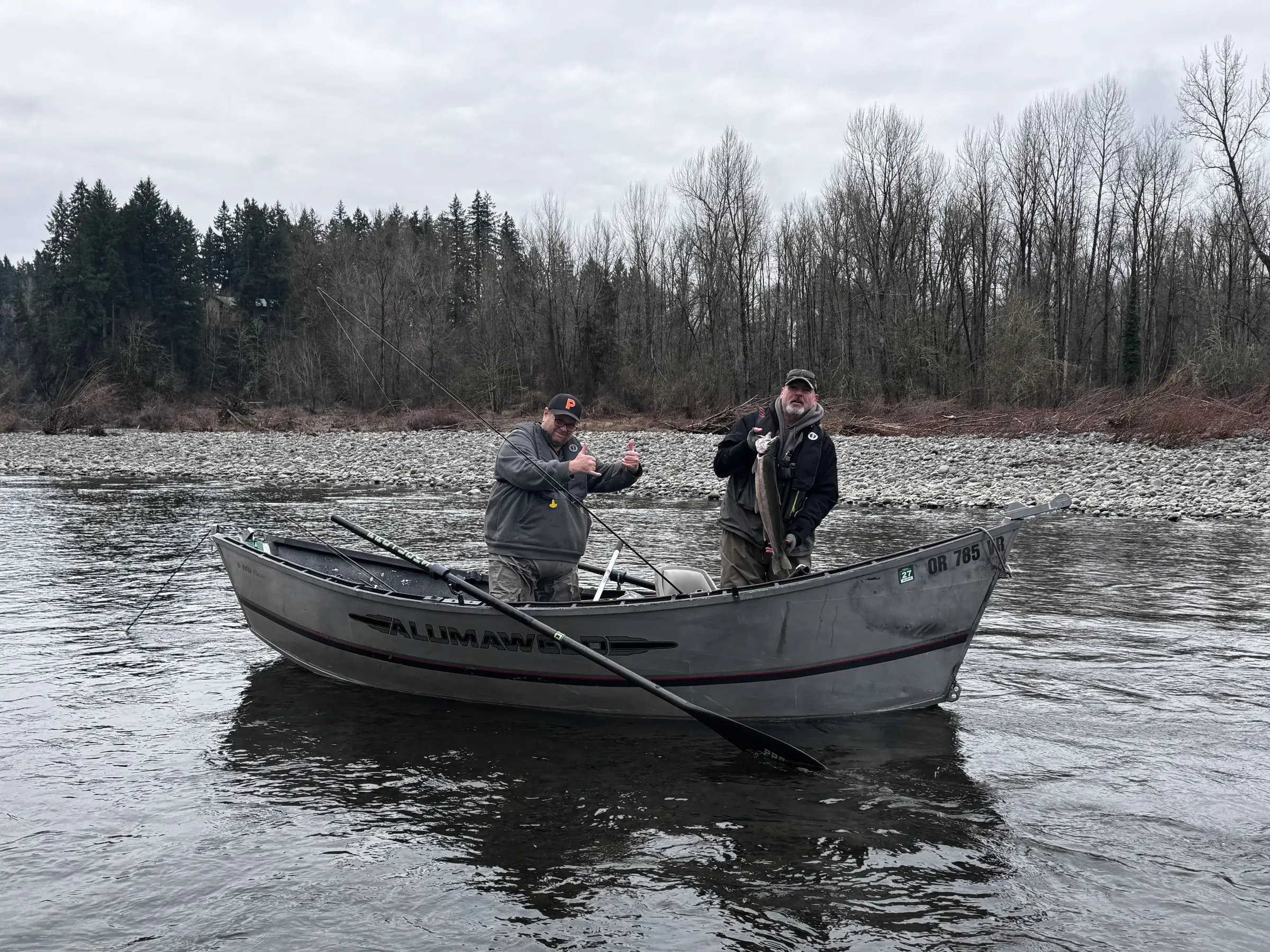 Two anglers standing in an Alumaweld drift boat on a wide river, one holding a fish