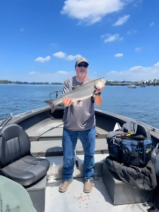 Angler standing on a boat holding a fish under a blue sky