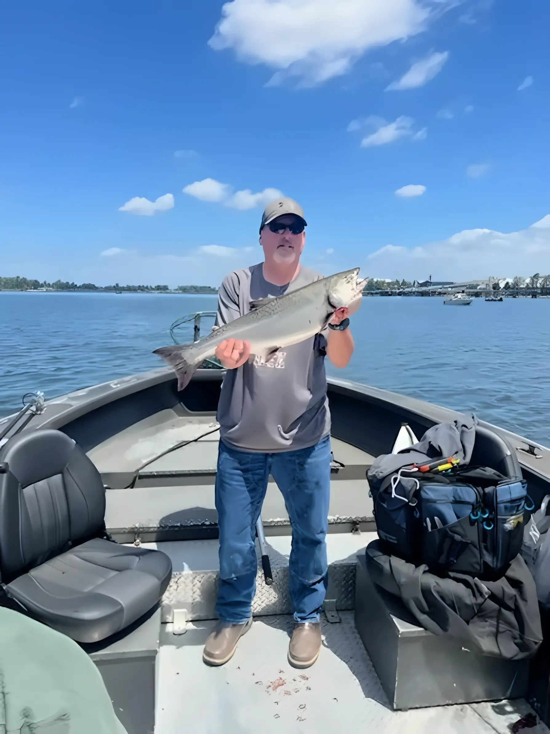Angler standing on a boat holding a fish under a blue sky
