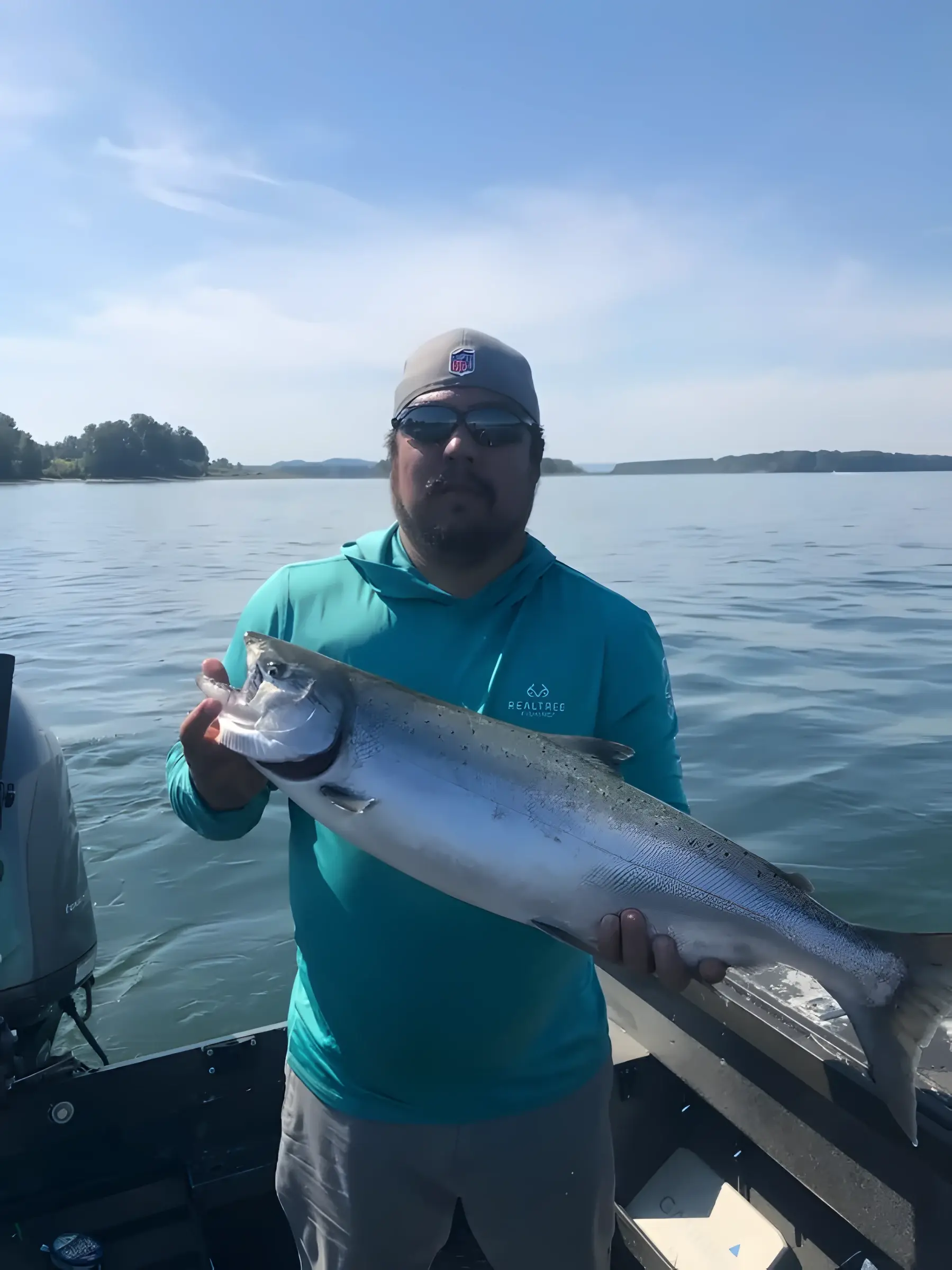 Angler in a teal shirt holding a large fish on the water