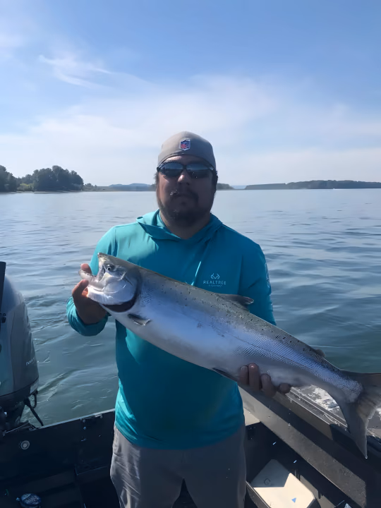 Angler in a teal shirt and sunglasses holding a large fish on the water