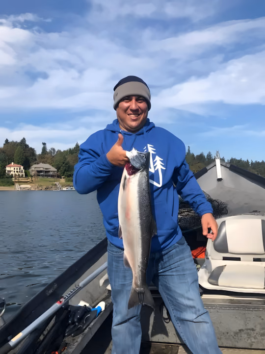 Smiling angler in a blue hoodie giving a thumbs-up while holding a fish