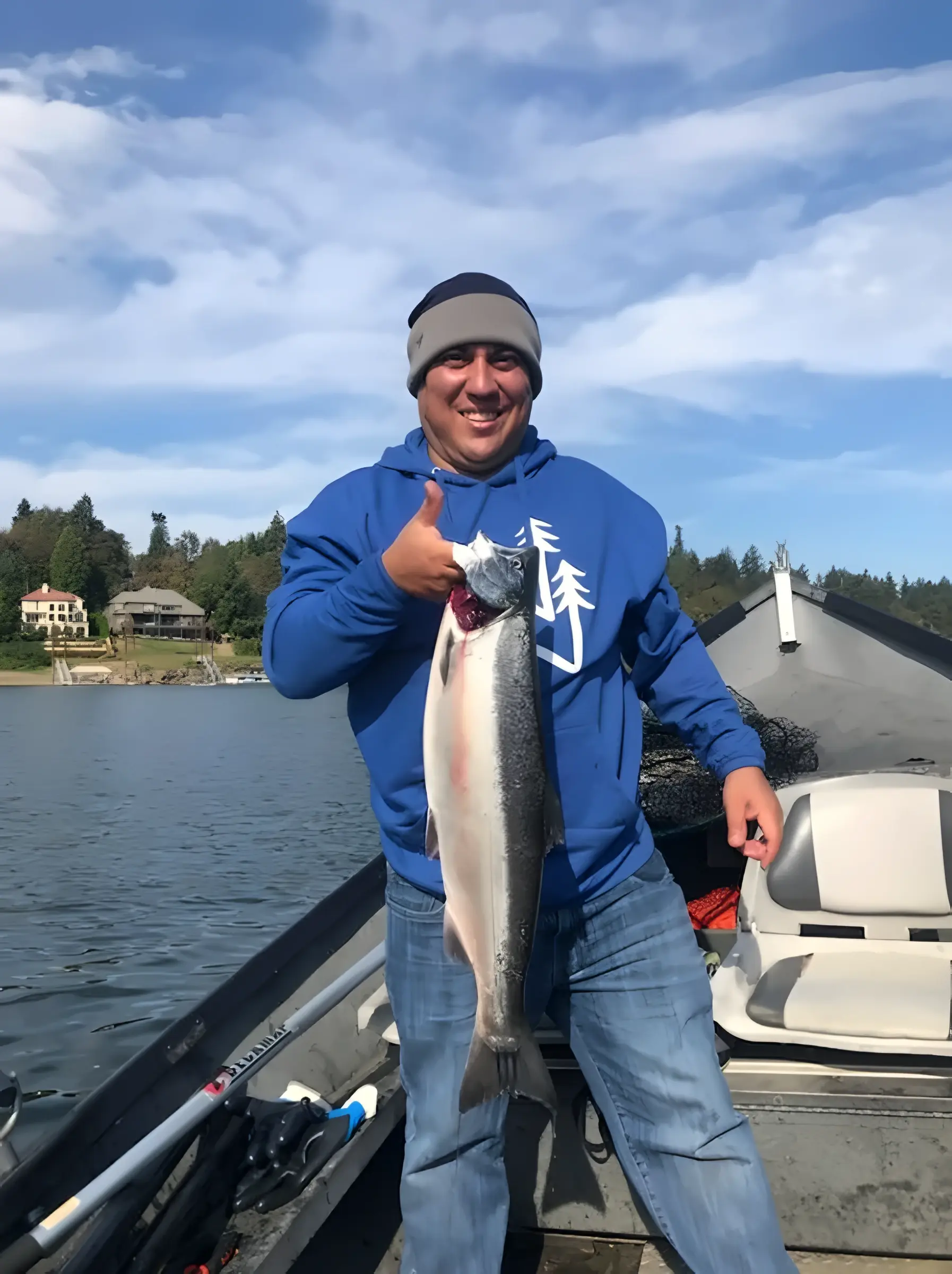 Smiling angler in a blue hoodie giving a thumbs-up while holding a fish