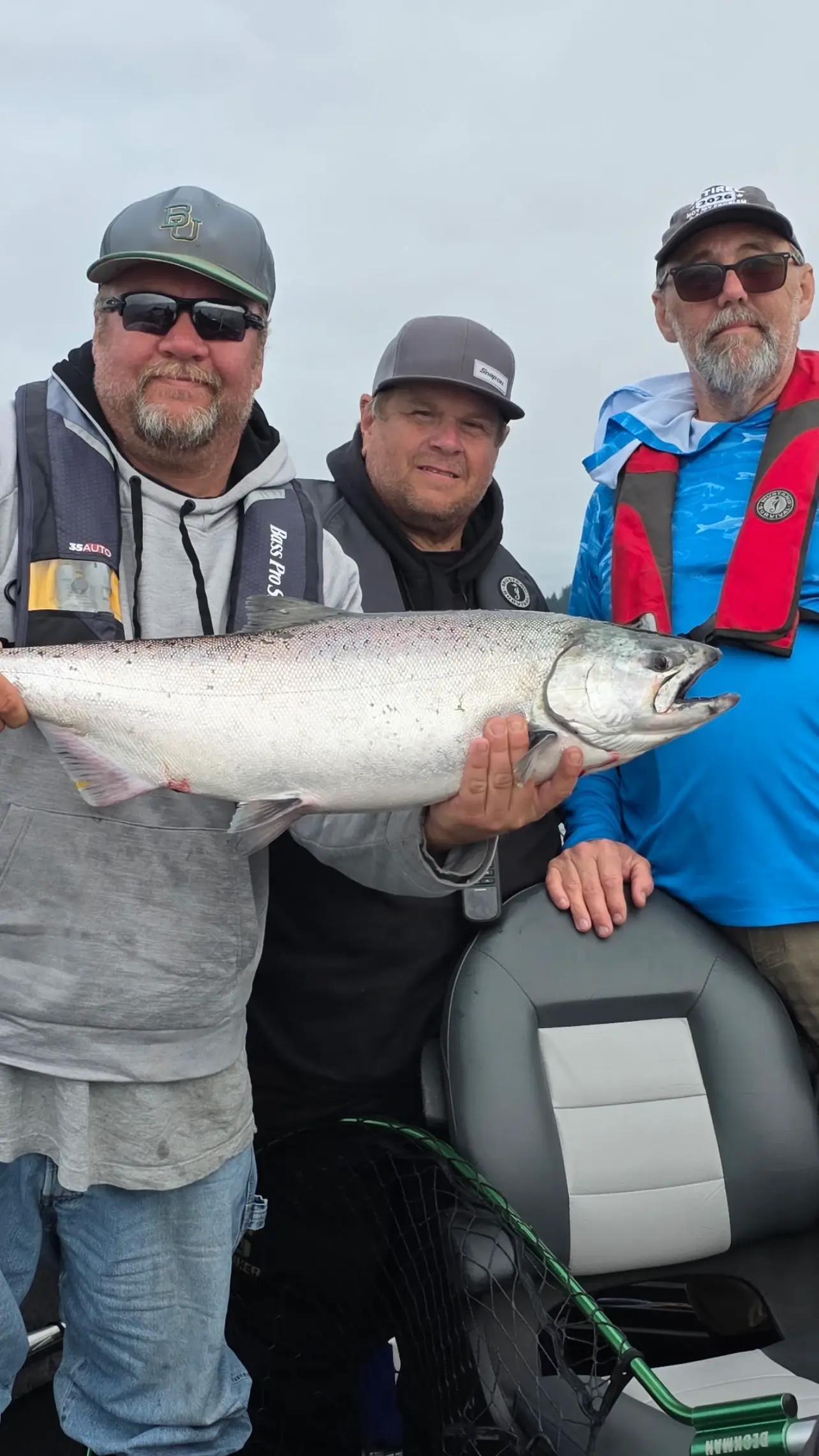 Three anglers in life jackets on a boat holding one large fish between them