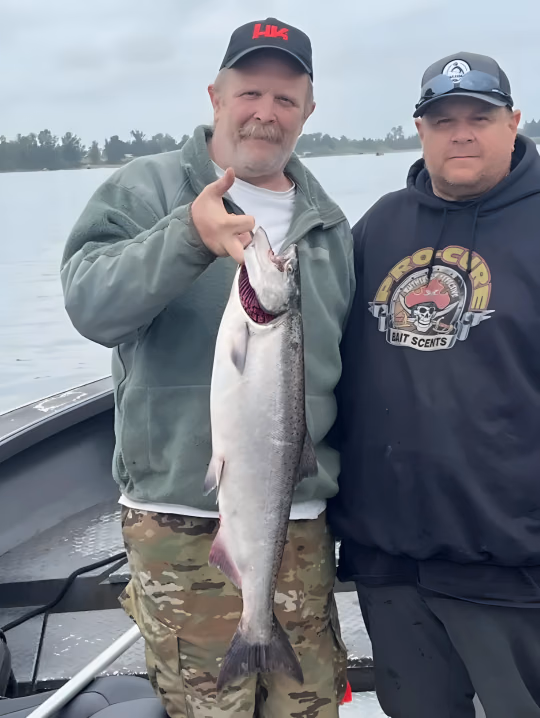 Two anglers on a boat, one holding a large silver fish