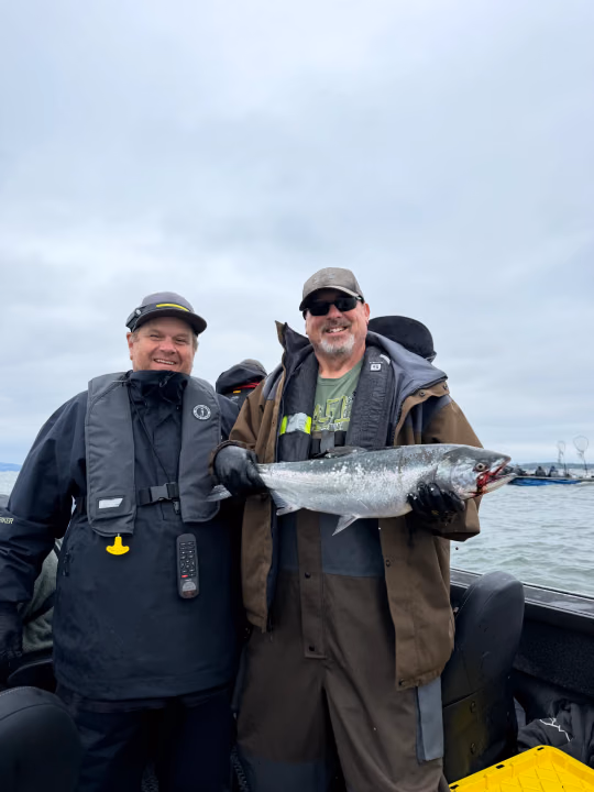 Two anglers in rain gear smiling on the boat, one holding a fish