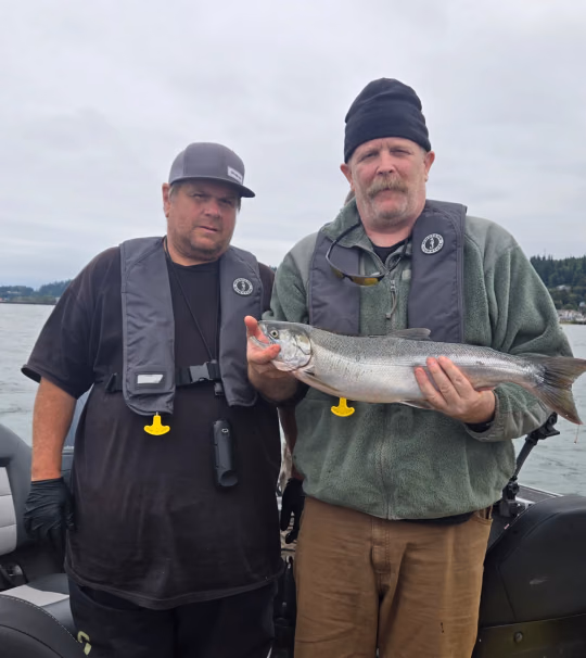 Two anglers in inflatable life vests on a boat, one holding a fish