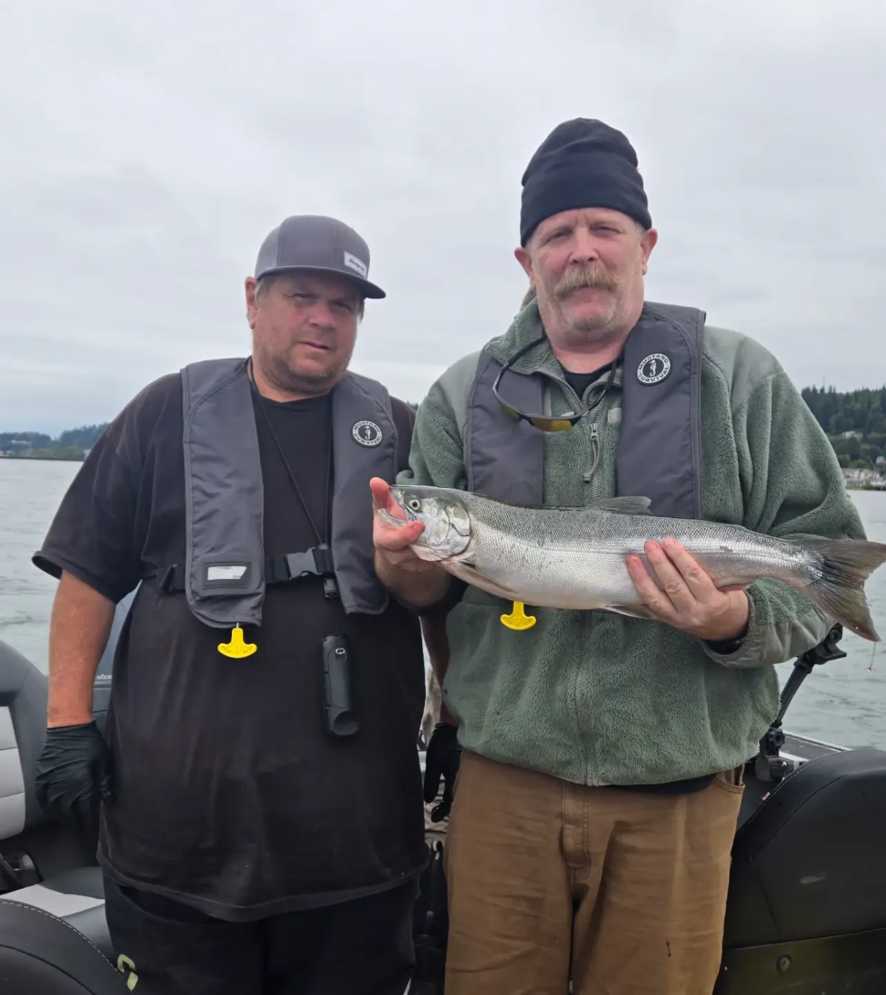 Two anglers in inflatable life vests on a boat, one holding a fish