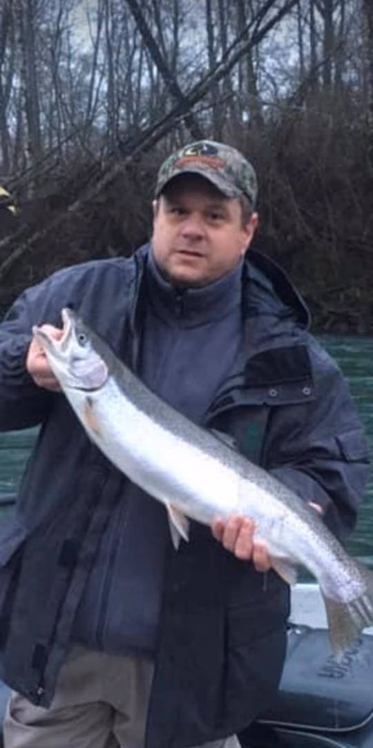 Angler in a camo cap holding a fish, bare winter trees behind