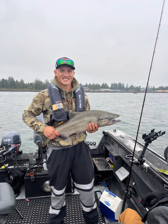Young angler in camo and waders holding a large fish on the boat